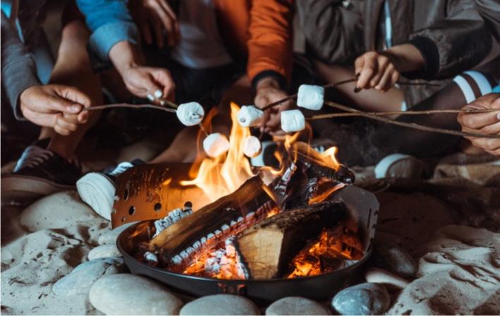 hands holding sticks to roast marshmallows over outdoor fire